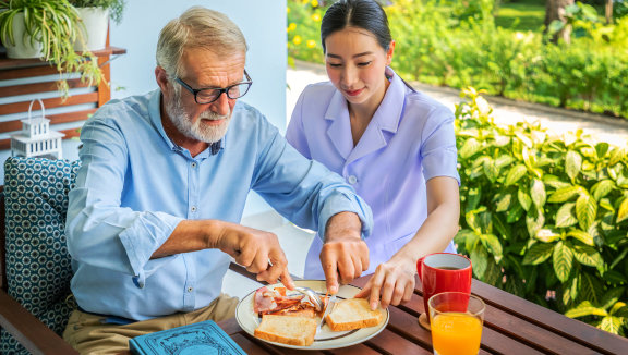 female caregiver assisting an elderly man cutting a sandwich