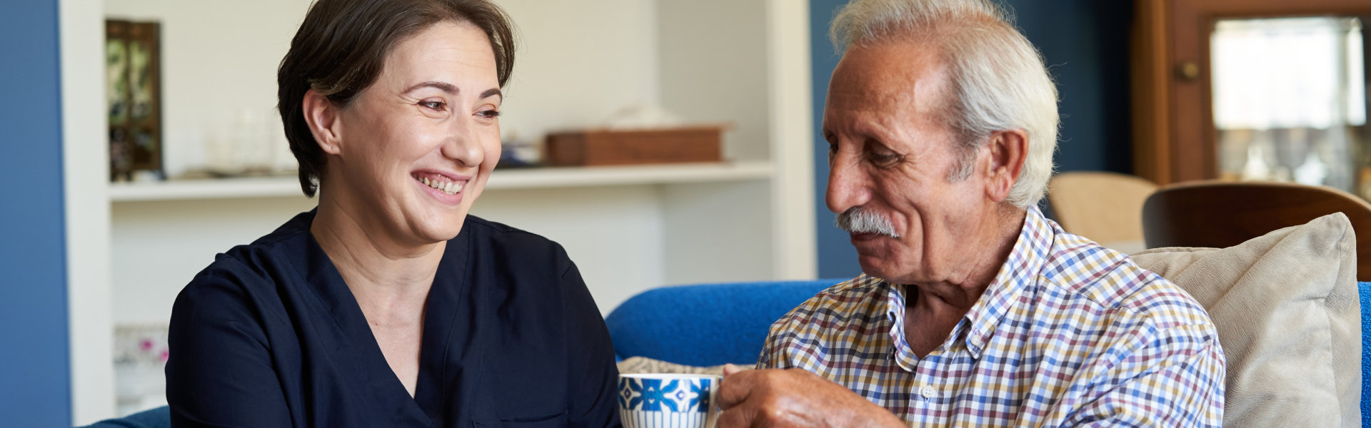 female caregiver smiling at elderly man drinking tea